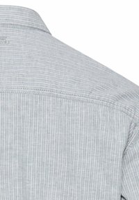 Zbliżenie na tył jasnoszarej koszuli z pionowymi białymi paskami i widocznym przeszyciem szwów na ramieniu.