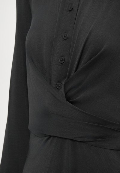 Zwarte wikkeltop met een knoopsluiting, een gestructureerde stof en een kruisontwerp op de taille. Zachte, vloeiende silhouet met lange mouwen.
