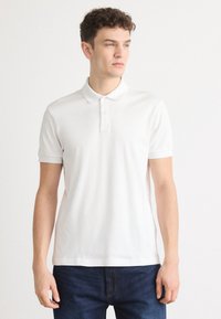 Hvit polo skjorte laget av lett stoff, med klassisk krage, tre knapper og korte ermer. Diskret logodetalj på brystet.