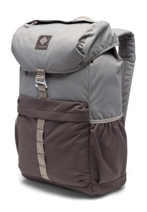 Ung kvinde i sort skjorte og grønne shorts iført en stor tofarvet grå vandrerygsæk, stående sidelæns på hvid baggrund.