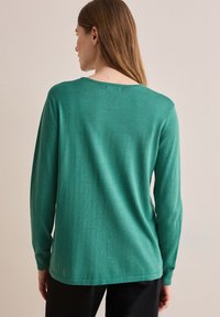 Langärmliger, tiefgrüner Pullover aus weichem Stoff. Mit einem runden Ausschnitt, figurbetonten Ärmeln und einer leicht lockeren Passform.