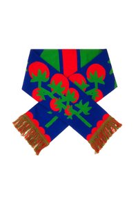 Dzianinowy szalik z niebieskim tłem, czerwonym wzorem kwiatowym i zielonymi liśćmi oraz dekoracyjnym frędzlem w zielonym i czerwonym na końcach.