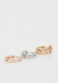 Tre metallringar: en roséguld med en ensam sten, en silverring med små stenar och en guldring med diagonala stenslingor.