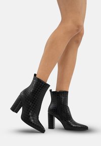 Botas de tobillo negras con un patrón de tablero de ajedrez texturizado, punta afilada y un tacón grueso. Cuenta con una cremallera lateral para el cierre.