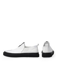 Weiße Slipper aus strukturiertem Leder mit einer schwarzen Gummisohle. Verfügt über einen grauen Akzentstreifen und eine Zuglasche an der Ferse.