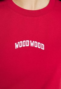 Röd bomullströja med rund halsringning och korta ärmar. Har vit text "WOOD WOOD" i en böjd design på bröstet.