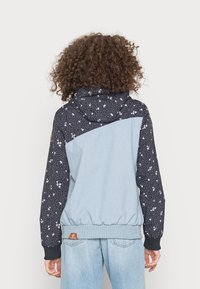 Sweatshirt com capuz, apresentando uma frente azul e mangas escuras com padrões florais, tecido texturizado e punhos e bainha elásticos.