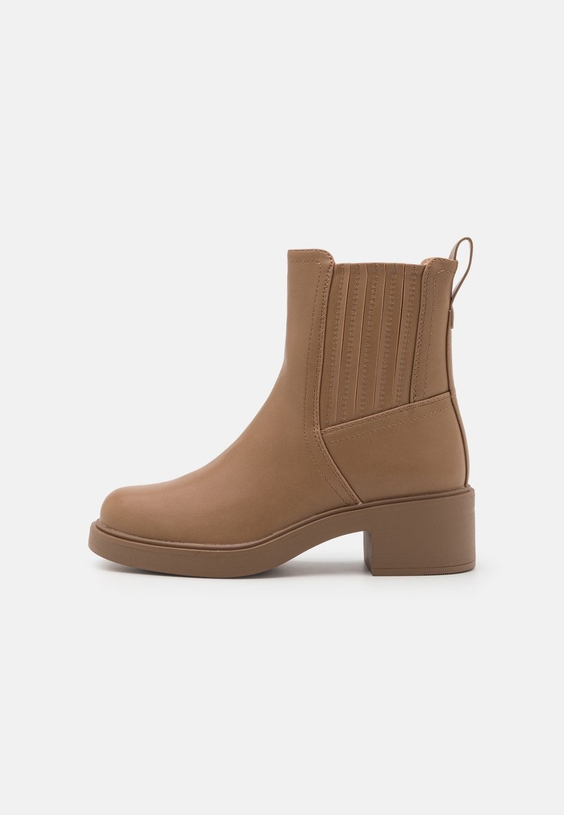 Světle hnědá kotníková bota s nízkým blokovým podpatkem, elastickou boční částí a poutkem na bílém pozadí, zobrazená z vnější strany.