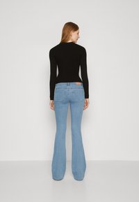 Top de manga larga negro acanalado combinado con jeans de campana azul claro que presentan bolsillos traseros y una etiqueta de cuero marrón en la cinturilla.