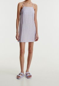 Lila sukienka bez rękawów z kwadratowym dekoltem, zdobiona małym kwiatowym wzorem. W połączeniu z jasnofioletowymi sandałami na klamrę. Gładka tekstura.