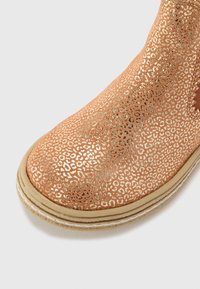 Botín de tobillo de cobre con un patrón texturizado que recuerda a las manchas de un leopardo. Presenta una puntera redondeada y una suela de goma beige cosida.