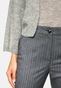Gray knit cardigan over a light gray sweater, paired with dark gray pinstriped trousers featuring a black button at the waist.