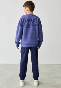 Tumesinine kapuutserekiga, mille seljaosas on "BAKER" tekst, kombineeritud sobivate cargo-pükste ja valgete tossudega, millel on logo kandadel.