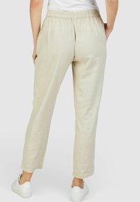 Beige linnen broek met een elastische tailleband, rechte snit, zijzakken en subtiele textuur, gecombineerd met witte sneakers.