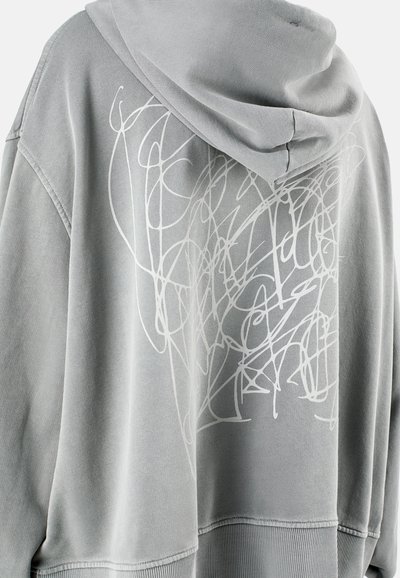 Szara, oversize bluza z kapturem, wyposażona w sznurki. Na plecach znajduje się abstrakcyjny wzór z białych linii. Wykonana z miękkiego materiału, z ściągaczem u dołu i przy mankietach.