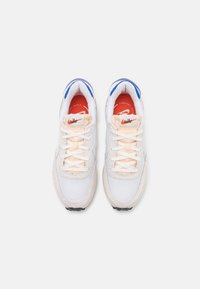 Baskets en mesh blanc avec accents en daim gris clair, comprenant des détails bleus, des semelles intérieures orange, et des lacets blancs. Semelle en caoutchouc noire.