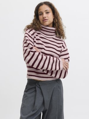 Sweter typu golf w pionowe paski w jasnoróżowym i burgundowym kolorze, o luźnym kroju i miękkiej fakturze. W zestawie z szarymi spodniami w kant o wysokim stanie.