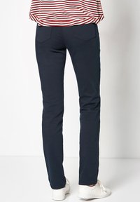 Navyblauwe slim-fit broeken van een katoenmix, met achterzakken en gestikte details, gecombineerd met witte sneakers.