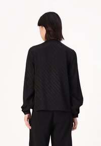 Black shirt with long sleeves, features a subtle dot pattern, relaxed fit, and elasticized cuffs; textured fabric.