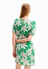 Zelené šaty s bílým květinovým vzorem, krátkými nafouklými rukávy, výstřihem na zádech a staženým pasem, vyrobené z lehké látky.
