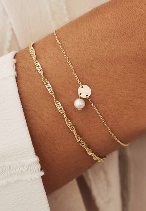 Goldene Kettenarmband mit einem verdrehten Glieddesign, akzentuiert mit einem runden Anhänger und einem einzelnen Perlencharme, getragen an einem Handgelenk.