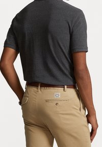 Mörkgrå kortärmad polo skjorta i kombination med khakifärgade byxor som har en bakficka och en logotypapplikation, framhävt av ett brunt bälte.