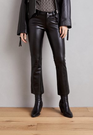 Pantalones acampanados de cuero negro con una textura suave, con bolsillos delanteros y cintura de altura media. Combinados con botines negros de tacón puntiagudo.