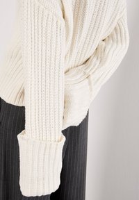 Maglione bianco lavorato a maglia con una trama a coste e maniche oversize. Dettagli notevoli includono ampie polsini e una vestibilità comoda.
