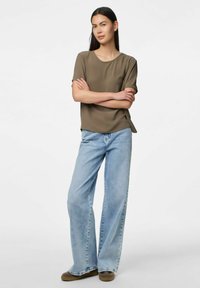 Top marrone a maniche corte con colletto rotondo, abbinato a jeans a gamba larga blu chiaro, caratterizzati da un lavaggio leggermente sbiadito e una vestibilità casual.