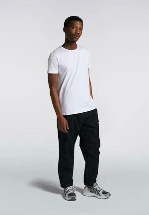 T-shirt bianco a maniche corte abbinato a pantaloni cargo neri, dotati di tasche. Modello che indossa scarpe sportive grigie con design a rete.