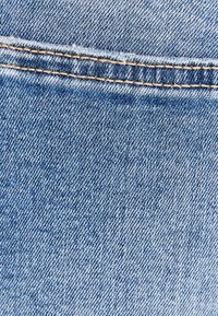 Ljusblå denimtyg med en distinkt twillbinding, som har en något blekt textur och kontrasterande sömnad längs sömmen.