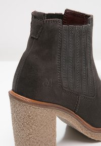 Harmaa mokkasaapikkaat, joissa on teksturoitu vaaleanbeige lohko korko ja elastiset sivupaneelit. Ominaisuuksia ovat pystysuora ommel ja pieni logotunnus.