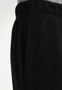 Pantalons de sport noirs au texture douce, dotés d'une taille élastique et de poches latérales. Le tissu semble lisse et durable.