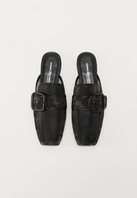 Mules en cuir noir avec un embout carré, dotés d'une sangle en dentelle noire texturée et d'une grande boucle rectangulaire en accent. Finition intérieure lisse.