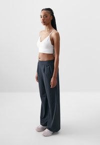 Bela rebrasta kratka majica, ohlapne tamne hlače in svetli športni copati. Outfit ima enostaven dizajn z minimalnimi akcenti in teksturami.