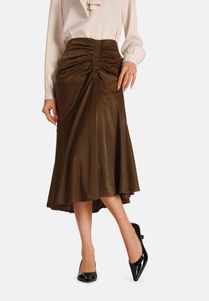Gonna midi marrone con texture arricciata in vita, design svasato, materiale liscio e orlo asimmetrico. Abbinata a tacchi neri a punta.