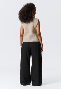 Beige, geripptes, ärmelloses Rollkragenpullover, kombiniert mit weit geschnittenen schwarzen Hosen. Das Outfit zeichnet sich durch eine strukturierte Verarbeitung und eine lässige Silhouette aus.