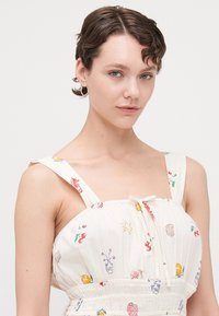 Vestido blanco con bordados coloridos, tirantes ajustables, lazo en la parte delantera y textura fruncida. Ideal para usar en climas cálidos.
