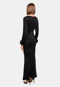 Schwarzes Langarmkleid mit figurbetonter Silhouette, aus Satinmaterial und mit Kunstfellmanschetten. Es hat eine elegante Rückennaht und einen hohen Schlitz.