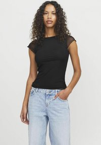 T-shirt nera aderente con maniche corte trasparenti, abbinata a jeans a vita alta blu chiaro. Tessuto liscio e silhouette classica.