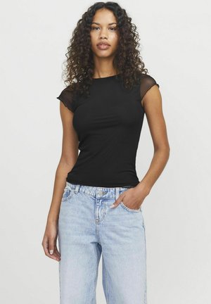 T-shirt nera aderente con maniche corte trasparenti, abbinata a jeans a vita alta blu chiaro. Tessuto liscio e silhouette classica.