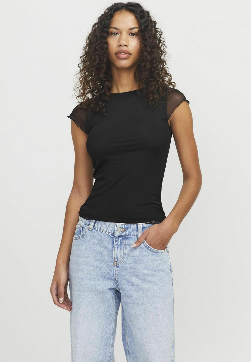 T-shirt nera aderente con maniche corte trasparenti, abbinata a jeans a vita alta blu chiaro. Tessuto liscio e silhouette classica.