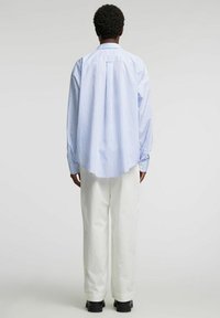 Blå og hvit stripet skjorte med knappestolpe, lange ermer og avrundet kant, kombinert med kremfargede bukser og svarte sko.