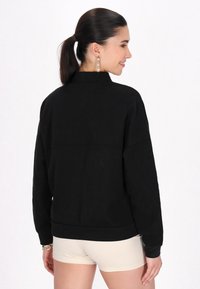 Schwarzer Sweatshirt mit entspannter Passform, gerippten Bündchen und Säumen; zeichnet sich durch eine glatte Textur und subtile Nähdetails entlang des Rückens aus.