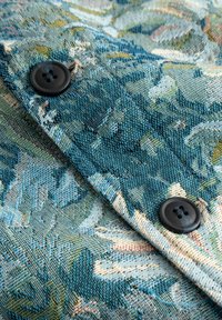 Tessuto a motivo floreale blu e verde con due bottoni rotondi scuri cuciti su strati sovrapposti di tessuto intrecciato.