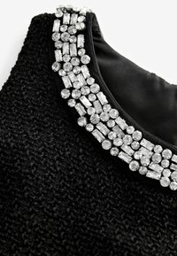 Encolure de robe en tissu texturé noir ornée de strass clairs ronds et rectangulaires regroupés.