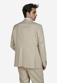 Beige maßgeschneiderte Sakkojacke mit einem Schlitz, glatter Textur und subtilen Steppdetails, von hinten gezeigt.