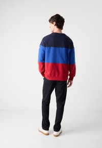 Color-blocked cotton sweatshirt featuring navy, blue, and red sections. Crew neck design, long sleeves, and ribbed cuffs.