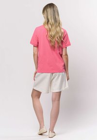 Ružové tričko s krátkym rukávom v relaxovanom strihu, doplnené svetlokrémovými šortkami. Tkanina je hladká, bez viditeľných vzorov alebo ozdôb.
