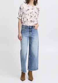 Blusa a maniche corte con motivo floreale in tessuto morbido, abbinata a jeans in denim a vita alta, a taglio ampio, di colore azzurro chiaro, e stivali alla caviglia marroni.